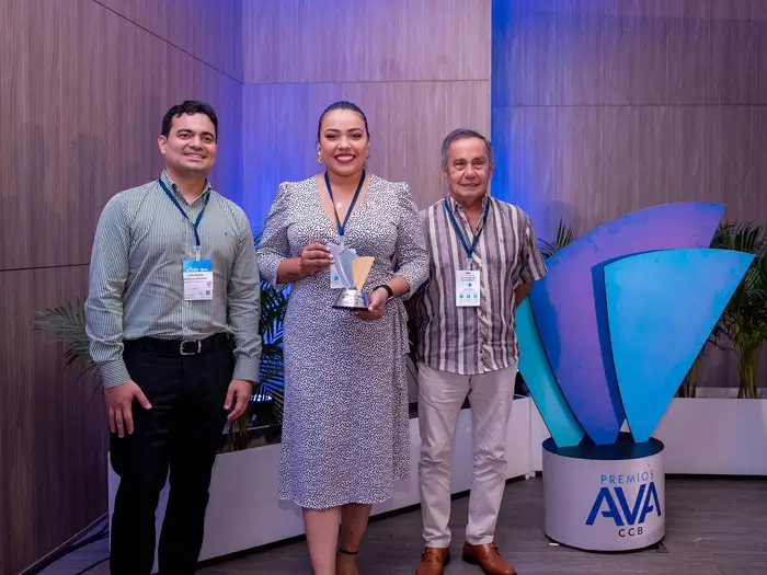 dos hombres y una mujer en medio quien sostiene premio AVA junto a los otros. 