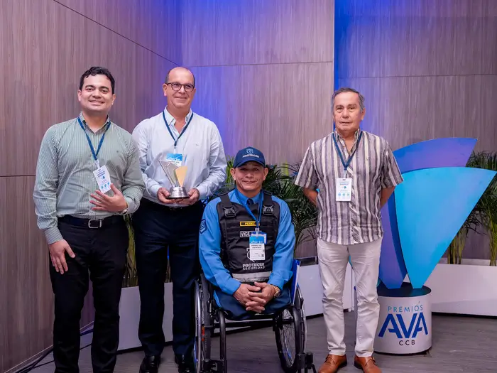 4 hombres, el hombre del centro en silla de ruedas que sostiene un premio AVA junto a los otros. 
